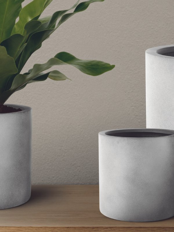 A collection of three different-sized ceramic pots in parchment and sage green tones, styled on a wooden bench in a sunlit room.